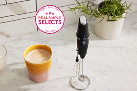 The ElitaPro milk frother on a counter next to a cup of frothed milk. 