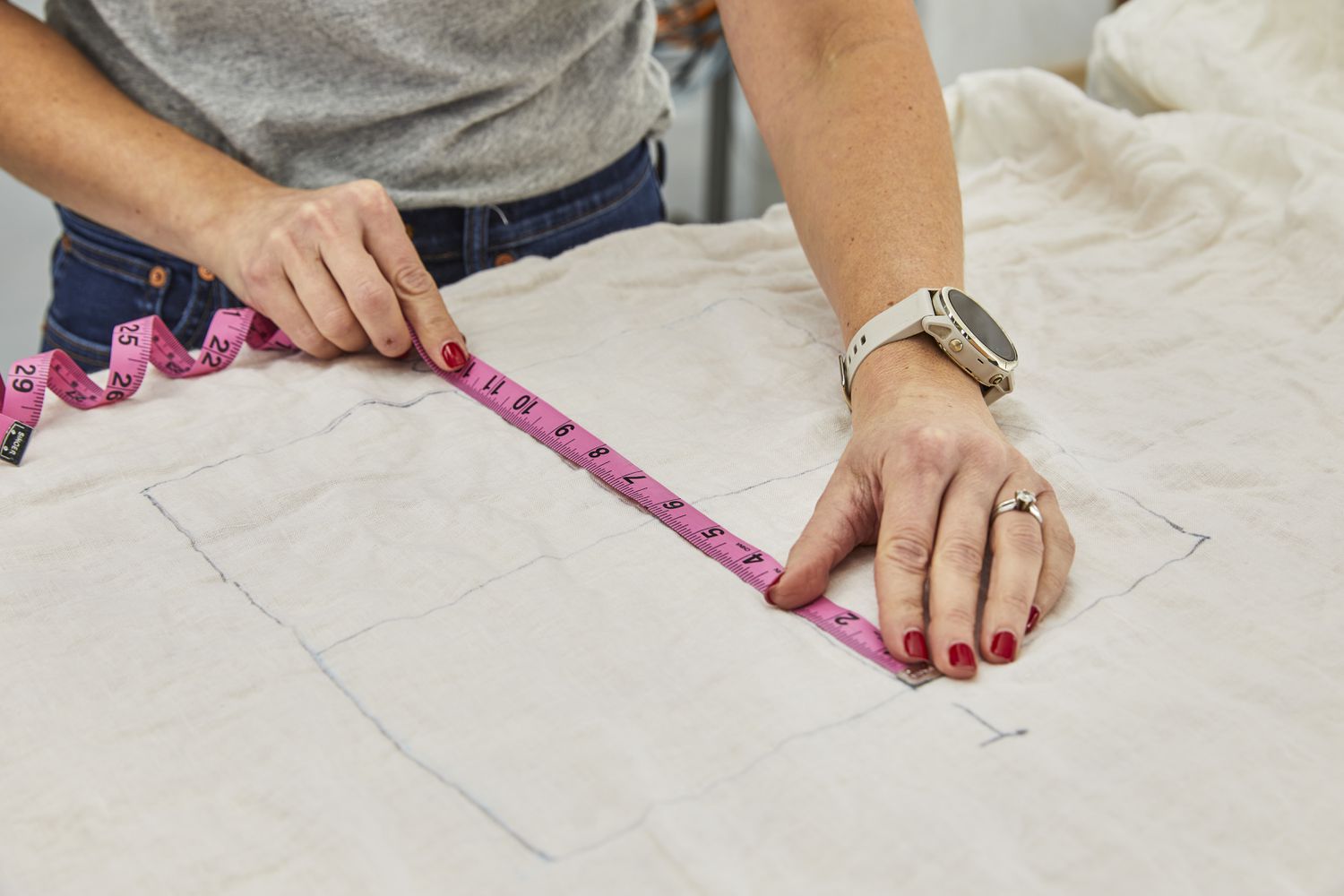 Hands using a measuring tape against a drawn out measurement on sheet material