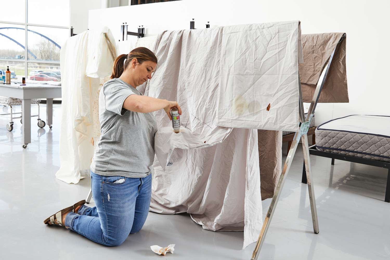 Woman kneeling and staining sheets from the Pact Cool-Air Percale Sheet Set hanging on a metal rack 