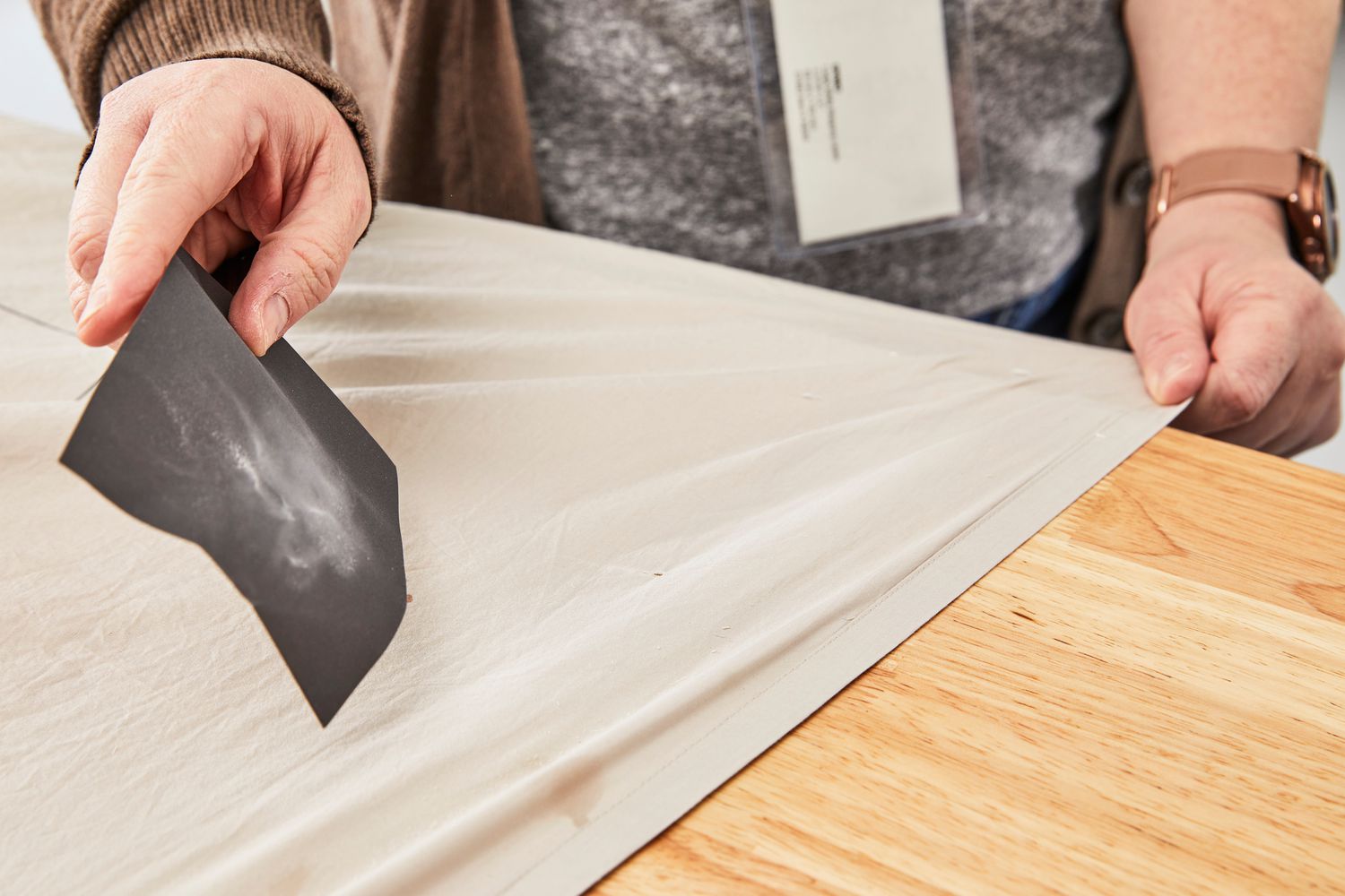 A person smoothing out the West Elm 400-Thread-Count Organic Percale Pleated Edge Sheet Set on a table