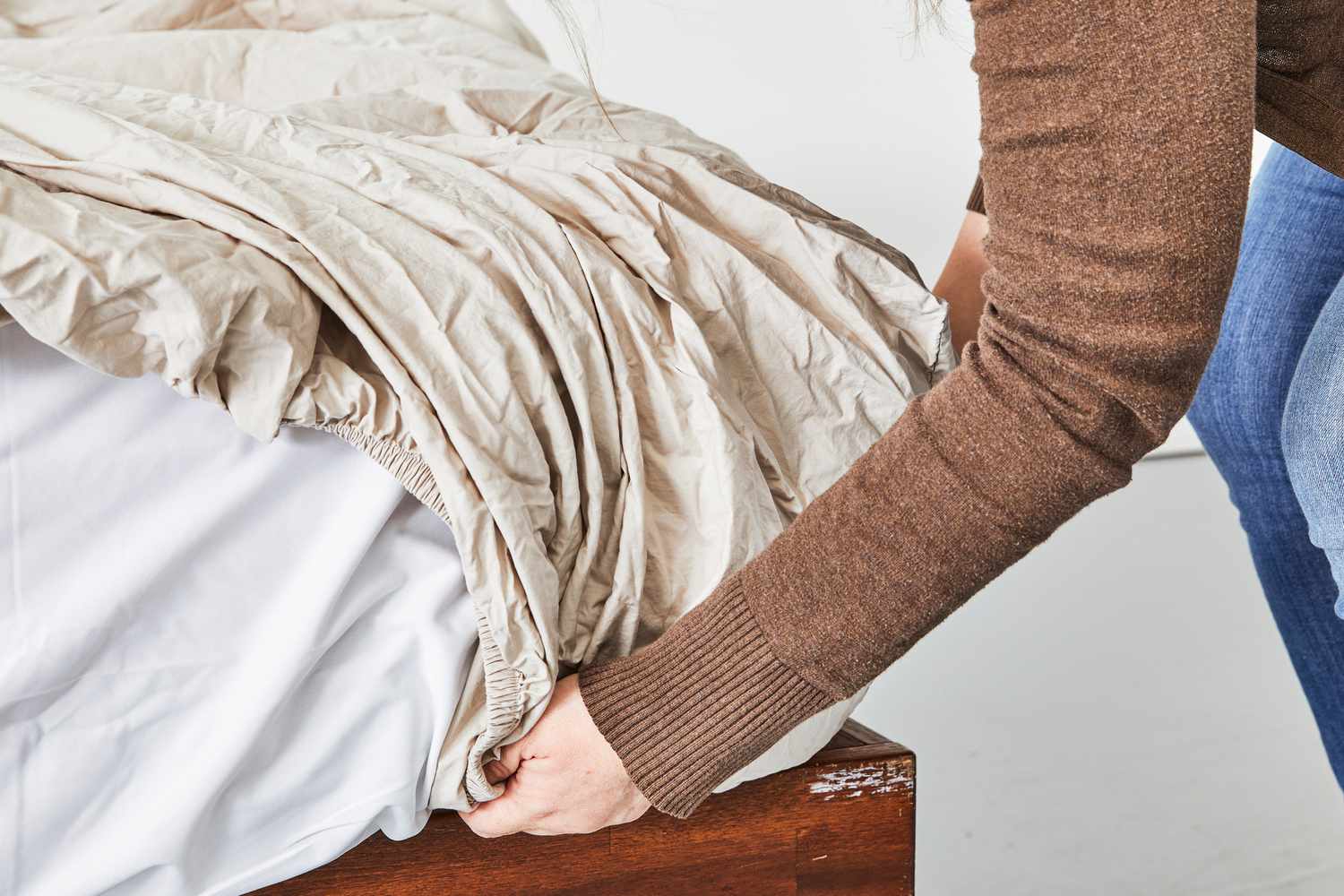 Close up of a person fixing a bed using the West Elm 400-Thread-Count Organic Percale Pleated Edge Sheet Set