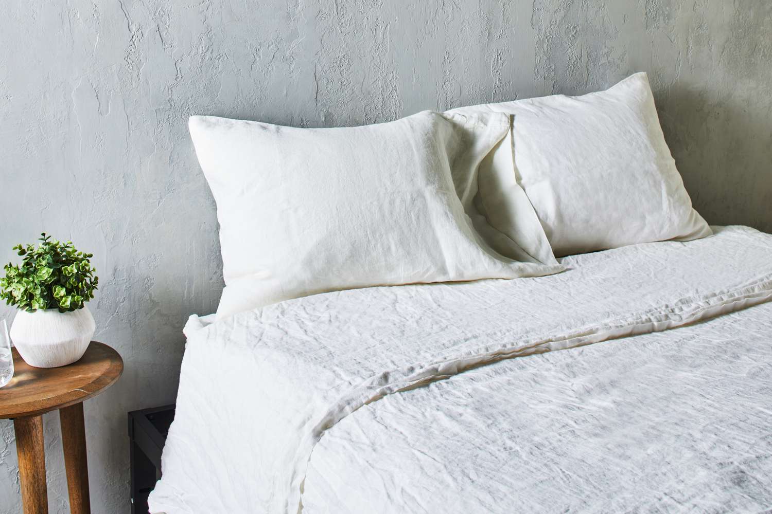 Pillows and mattress covered in Saatva Linen Sheet Set sheets and pillowcases next to a side table