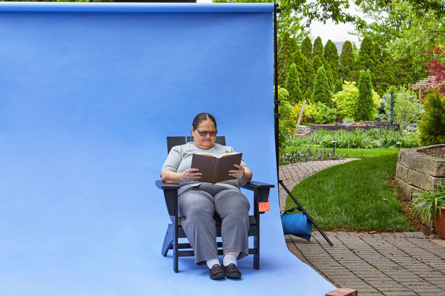 Person sitting on the Polywood Modern Adirondack Chair while reading a book in front of a blue screen