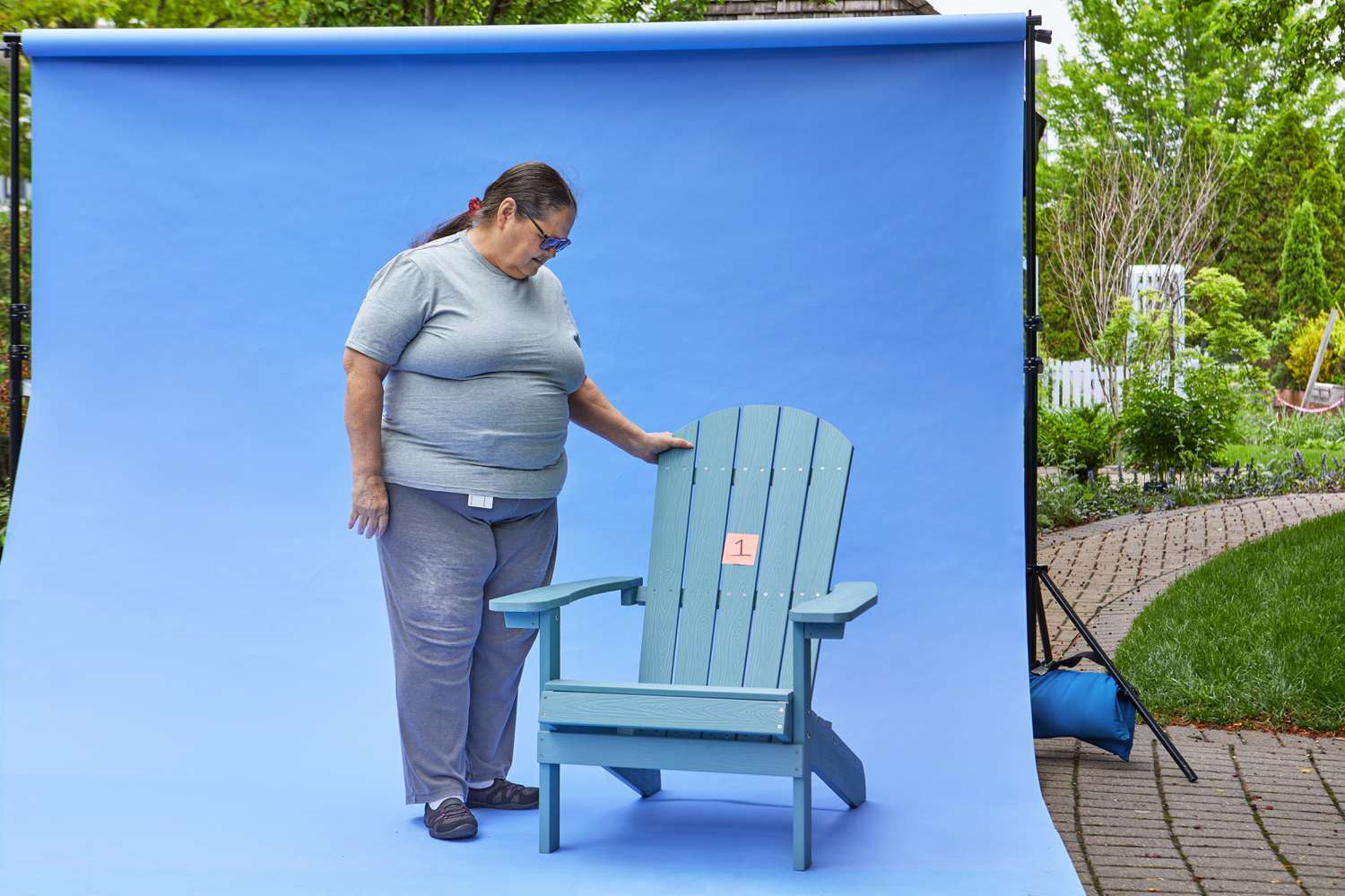 Woman stands next to a YEFU Adirondack Chair against a blue backdrop