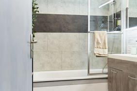 Bathroom interior with tub and tile in gray tones, towel hanging on glass shower doors.