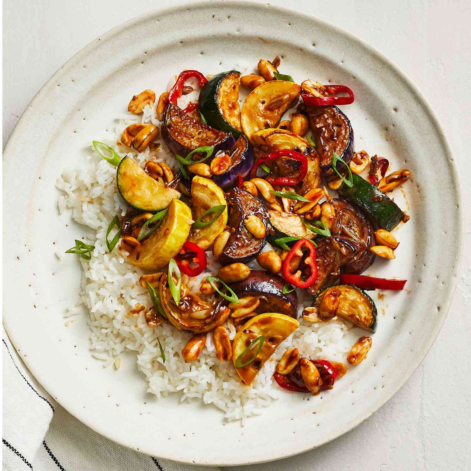 Spicy Summer Squash Stir-Fry With Eggplants, Served With White Rice on a White Plate