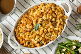 Cornbread Stuffing in a White Baking Dish on a Table with Mashed Potatoes, Gravy, and Green Beans