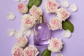 Bottle of perfume with rose flowers on color background, top view.