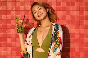 Vertical portrait of a cute chinese woman in swimsuit drinking a cocktail in a red urban background