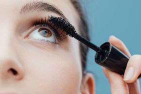 Woman applying mascara on her lashes, make up and cosmetics concept