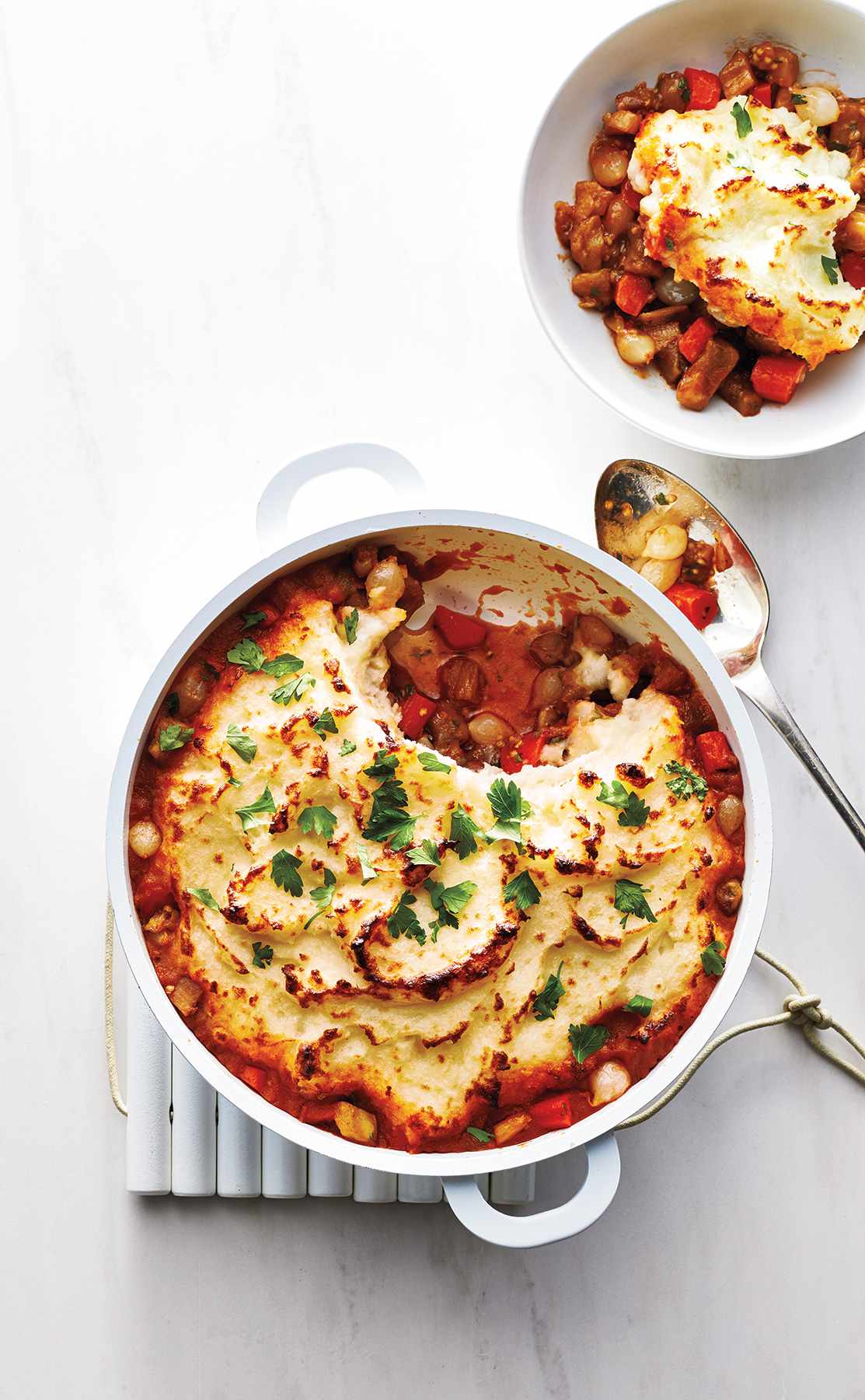 Vegetarian Eggplant Shepherd's Pie in a white pot with a small bowl of the dish and a metal spoon for eating