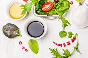 Salad preparation with oil and balsamic vinegar on white wooden table