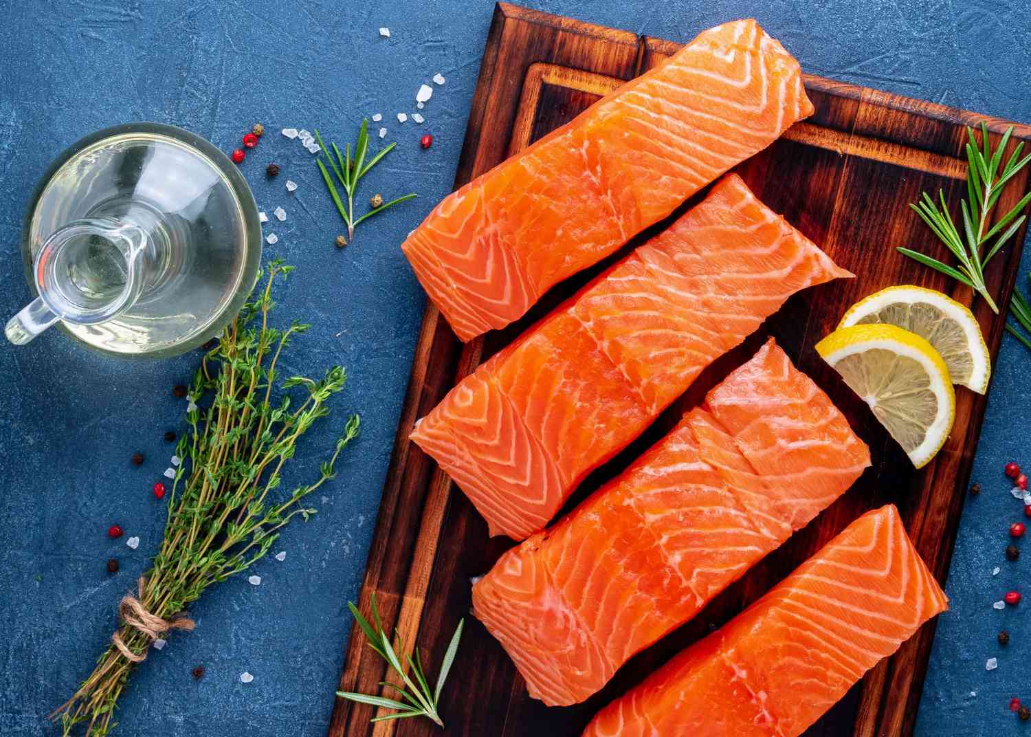 Food background, sliced portions large salmon fillet steaks on chopping board on dark blue concrete table, copy space, top view