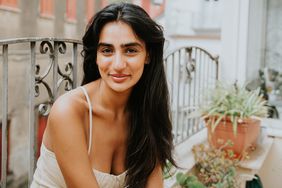 Simple portrait of a beautiful Indian woman on a European-style balcony with long wavy hair. She looks directly into the camera with a small smile.